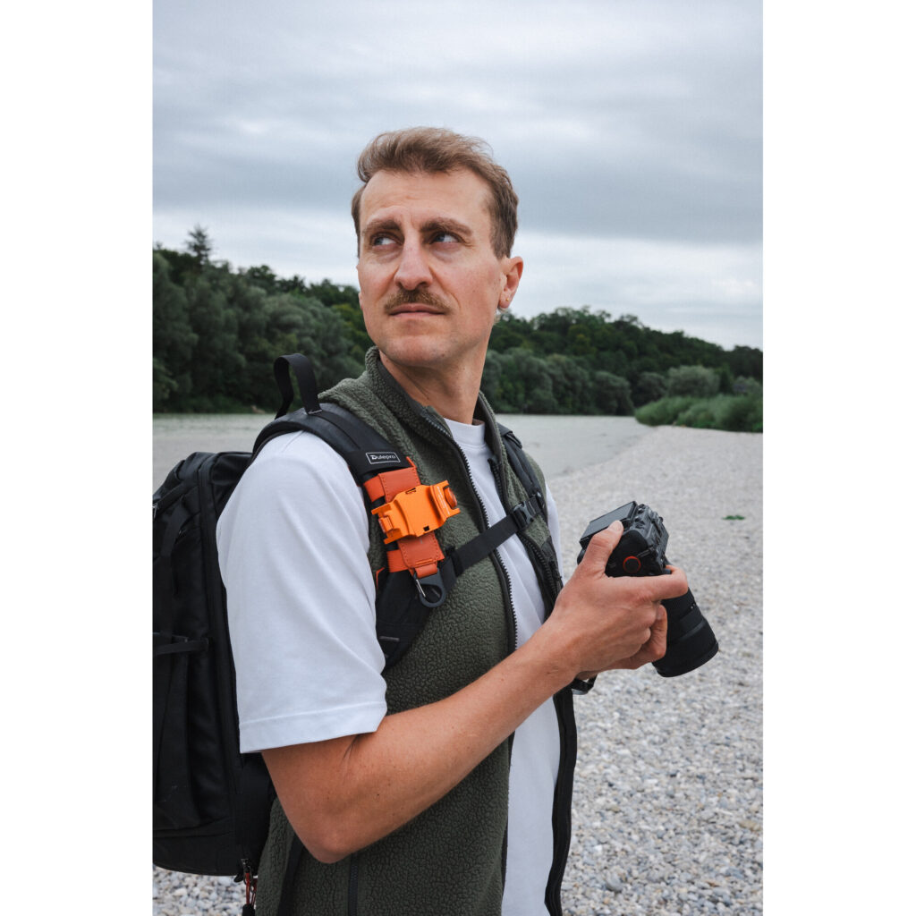 Summit-Creative Speedyclip-riem oranje bevestigd op rugzak tijdens gebruik met camera