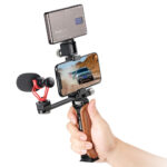 Leofoto VC‑1 handgreep in gebruik met smartphone, microfoon en LED‑lamp gemonteerd voor mobiele video‑opnamen.