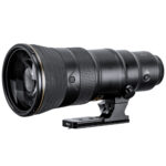 Leofoto NF‑01N objectiefvoet met grote Nikon telelens op lange statiefplaat geplaatst voor stabiele ondersteuning.