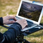 Leofoto LCH-2S laptophouder gebruiksvoorbeeld buiten met laptop op tray op statief terwijl de gebruiker typt.