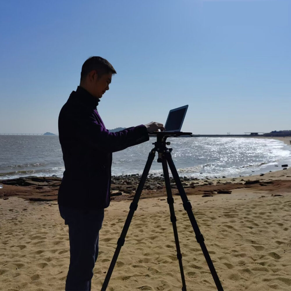 Leofoto LCH-2S laptophouder silhouet van fotograaf op strand die een laptop op statiefplatform bedient.