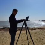 Leofoto LCH-2S laptophouder silhouet van fotograaf op strand die een laptop op statiefplatform bedient.