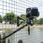 Leofoto MT-04 Tafelstatief met camera bevestigd aan hekwerk, poten om de spijlen gevouwen.