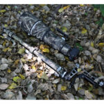 Leofoto LS-365CEX Tripod met camo PG-1 gimbal en telelens opgesteld tussen bladeren in het veld.