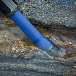 Leofoto LP-324C Tripod blauw statiefbeen in ondiep stromend water bij rotsachtige kust.