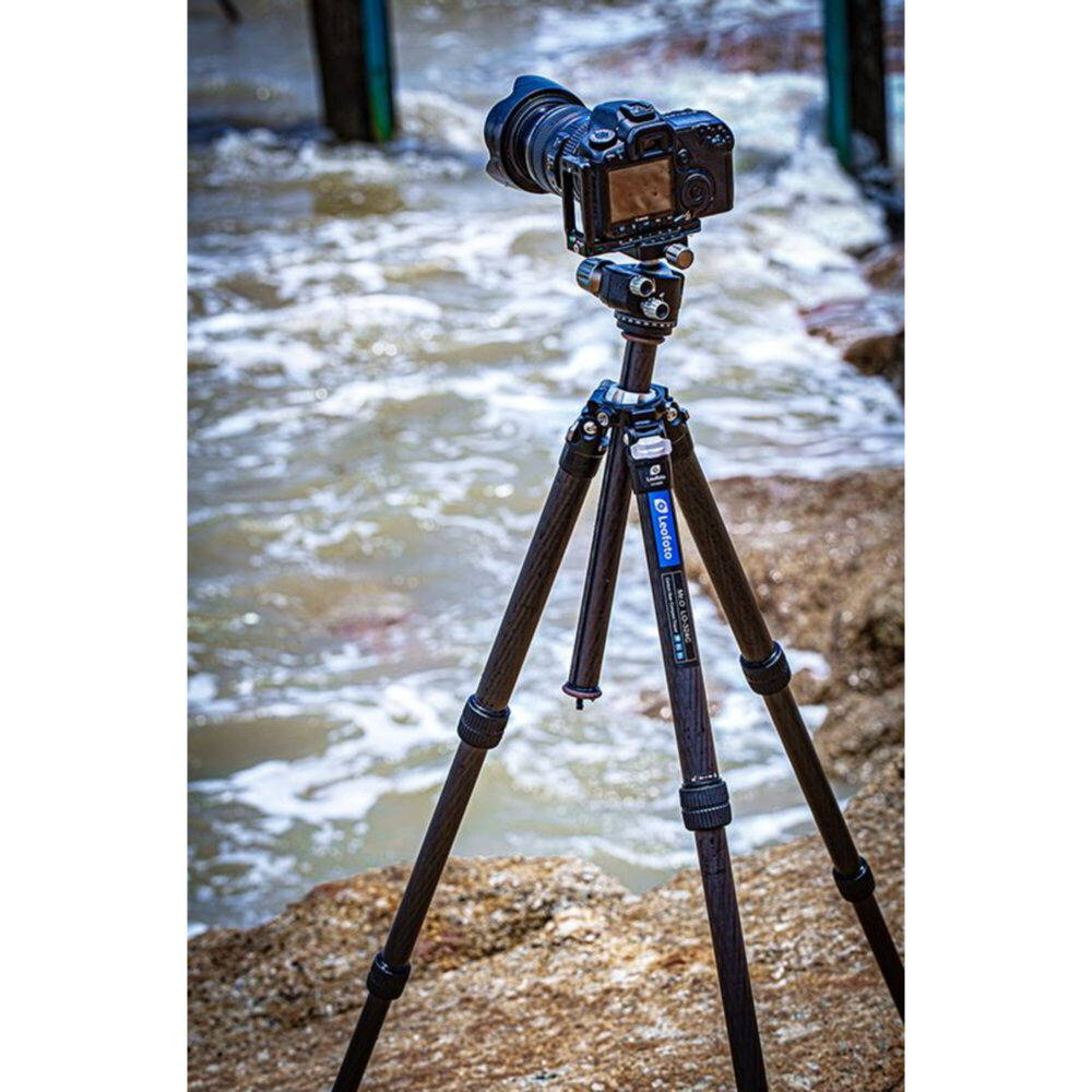 Leofoto LY-224C Tripod opgesteld in ondiep zeewater op kiezelstrand met camera gemonteerd.