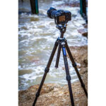 Leofoto LY-224C Tripod opgesteld in ondiep zeewater op kiezelstrand met camera gemonteerd.