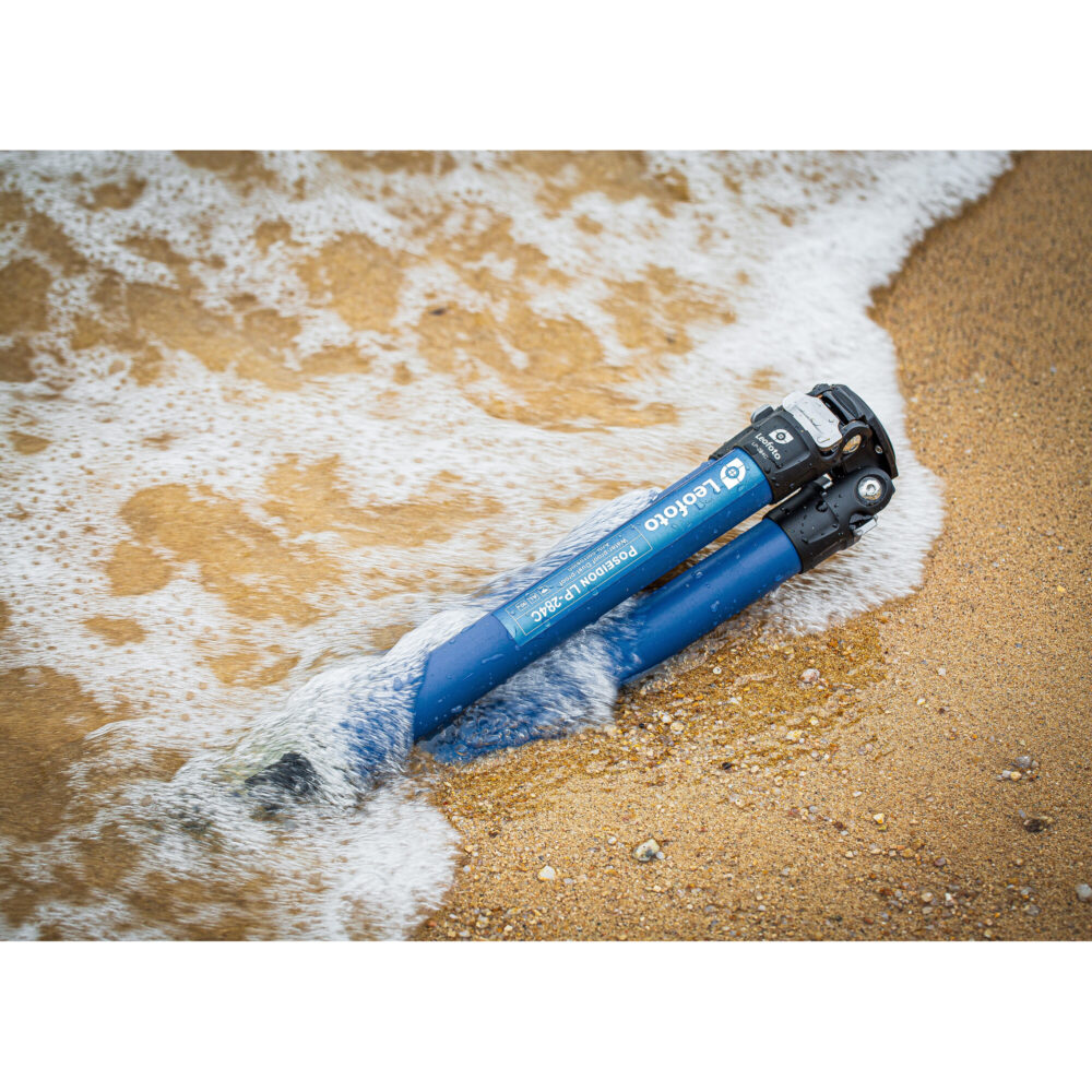Leofoto LP-284C Tripod statief liggend in nat zand aan zee met opspattend water voor kustfotografie.