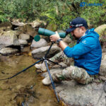 Leofoto LO-224CS Tripod laag opgesteld bij een beek met spotting scope voor stabiele observatie vanaf de oever.